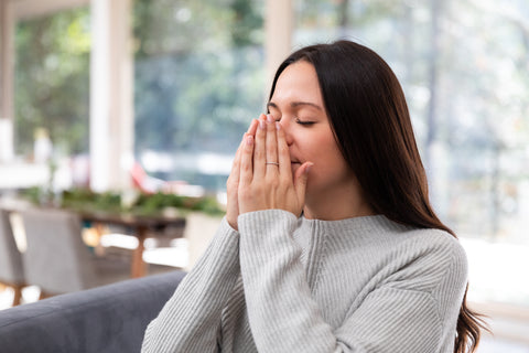 A woman cupping her hands around her nose and taking a deep breath