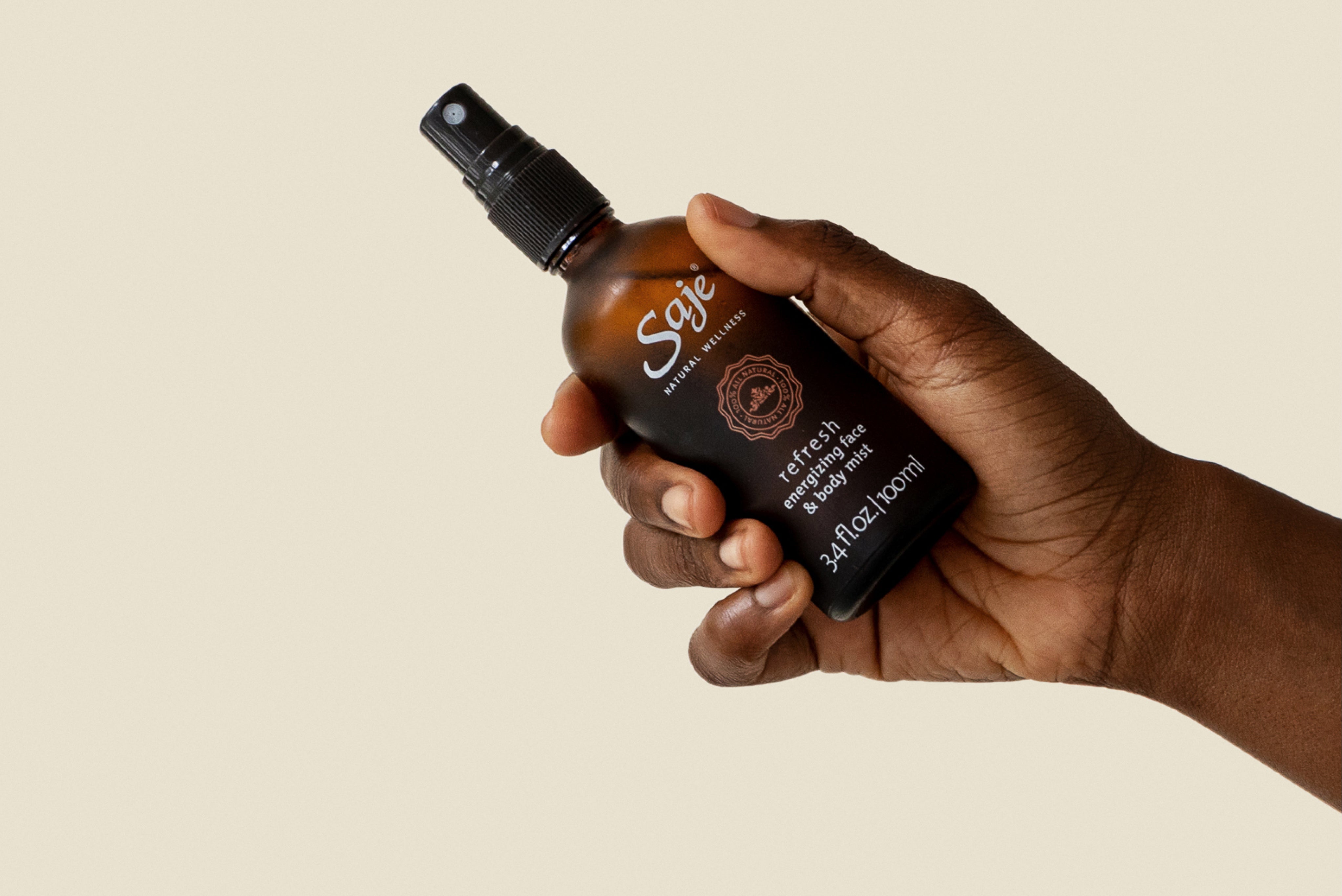 A hand holding refresh mist against a beige background