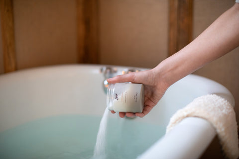 A hand pouring stress release bath salts to a bath tub