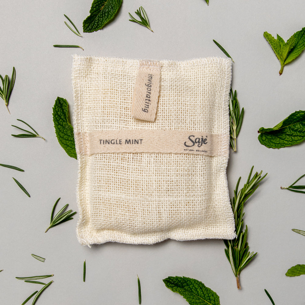 tingle mint jute wash pad surrounded by its ingredient scents including rosemary and mint on a pale blue background
