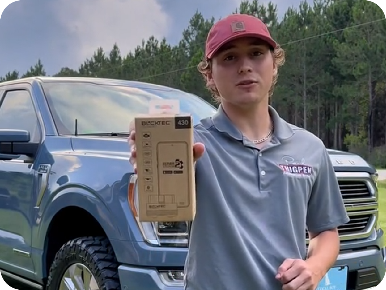 A young man standing in front of a SUV, holding a OBD2 scanner box
