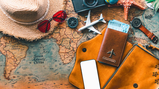  The image is a flat lay of travel essentials on a world map, including a straw hat, sunglasses, camera, compass, model airplane, passport holder, watch, and a starfish, suggesting an adventure or vacation theme.