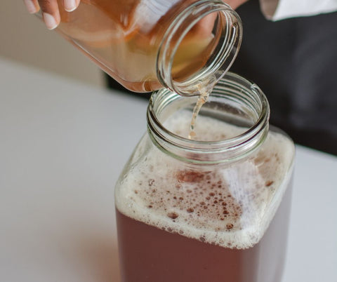 Someone pouring kombucha into a jar