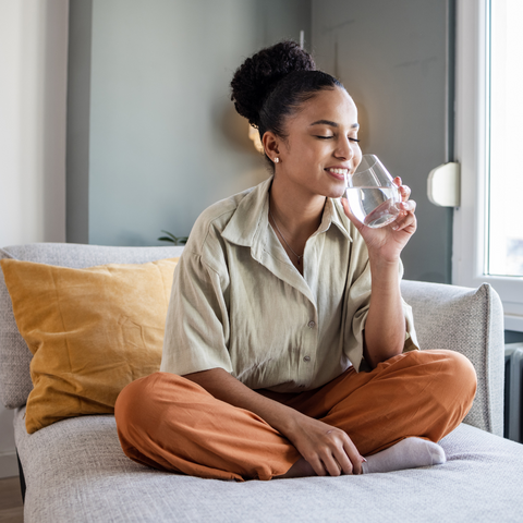 Woman sat on the sofa enjoying a glass of water