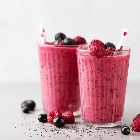 Two red smoothies in a glass with a straw topped with berries.