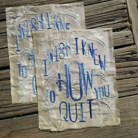 Matching back patches laid out on a weathered porch. They're made on an antique, salvaged silk that has a faint cream and beige floral print. The chainstitched lettering reads "I WISH I KNEW HOW TO QUIT YOU" in a western font, and the thread that makes up the lettering is a variegated blue, ranging from lite sky blue to a dark navy. 