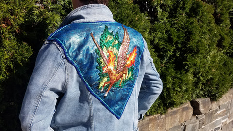 A full view of the pegasus back patch. The wearer is standing outside on a sunny day, in front of a row of bushes.
