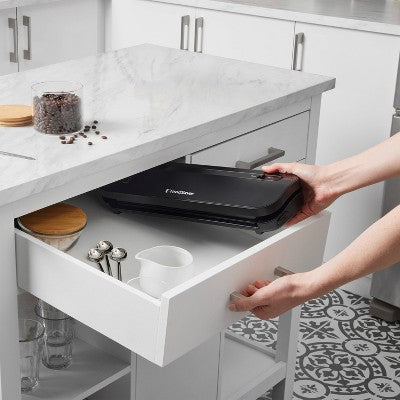 Person placing a compact vacuum sealer into a kitchen drawer with various utensils.