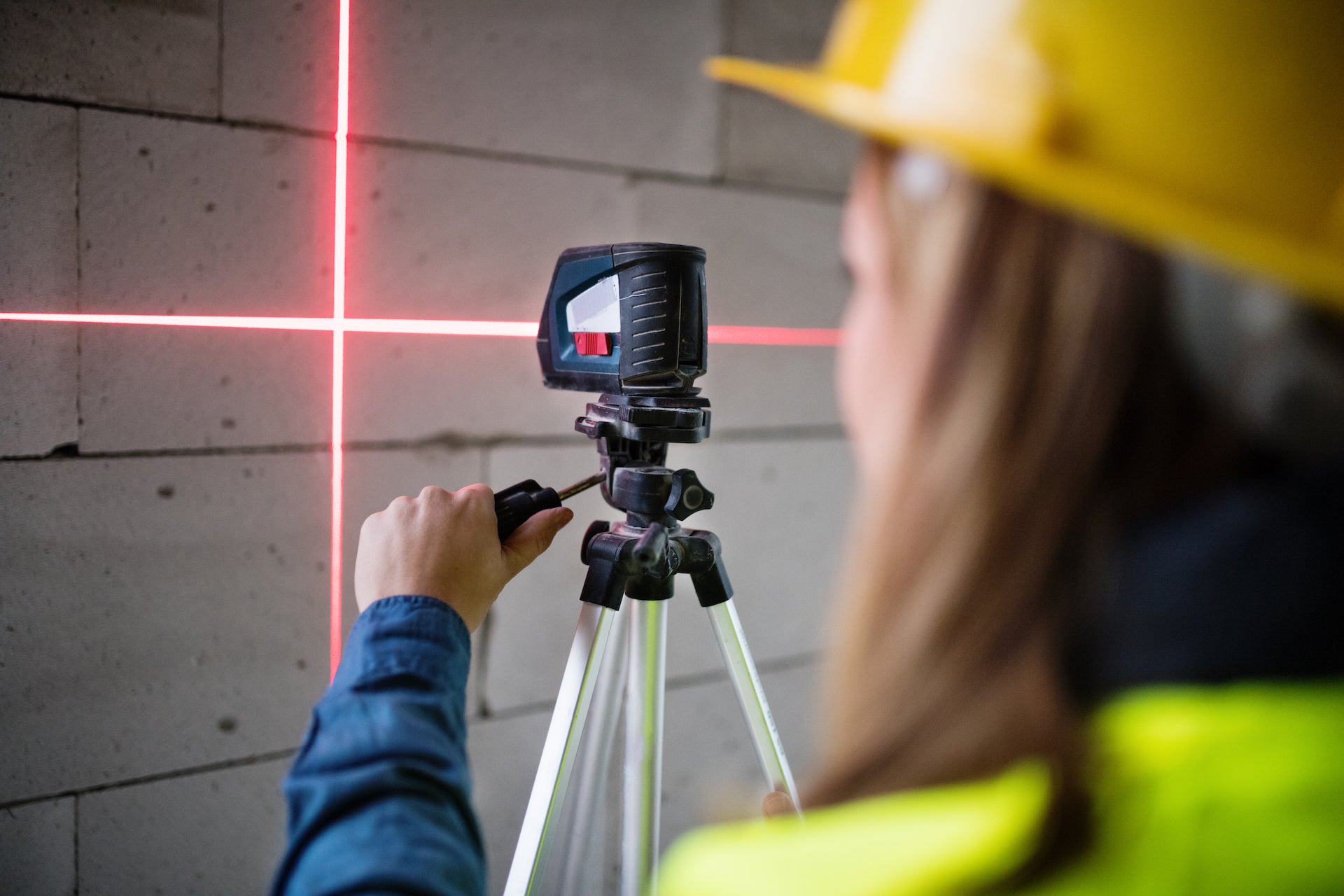 Construction worker using a laser level tool on a tripod.