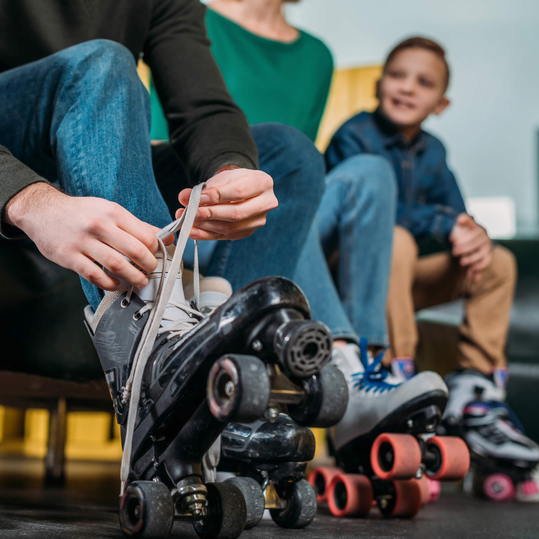 Person tying roller-skates while sitting next to two others in casual clothing.