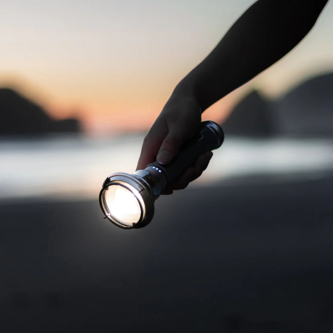 Hand holding a flashlight outside at dusk.