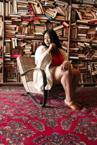 A plus size model sits in a library looking pensive