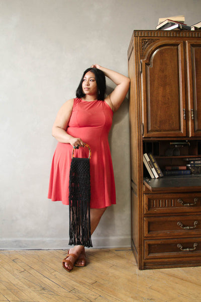 A plus size model leaning while wearing a sundress and holding a fringed handbag