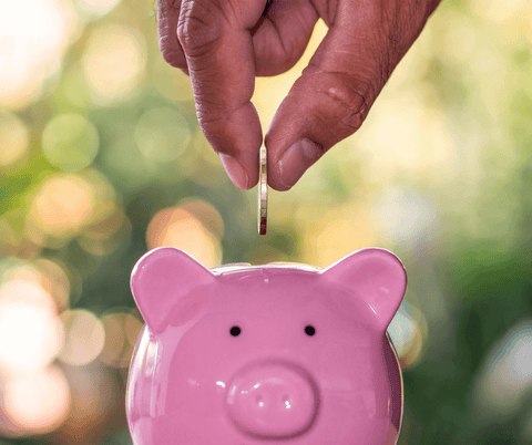 Close-up of a hand placing a coin into a piggy bank