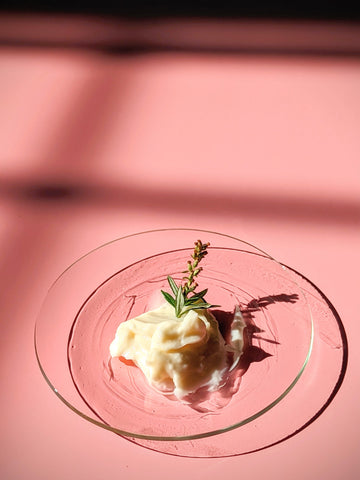 Creamy facial skin moisturizer on a pink background with a piece of mugwort on the cream.