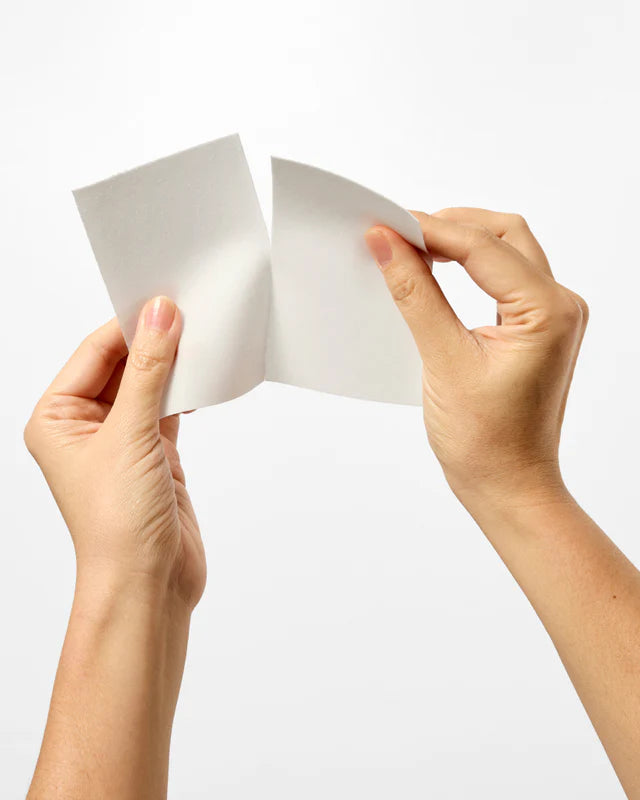 Hands tearing a white piece of paper in half.