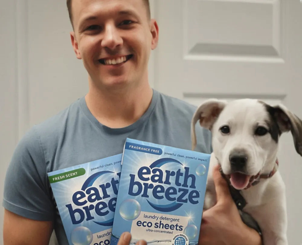 A smiling man holding a puppy and Earth Breeze laundry detergent packaging.