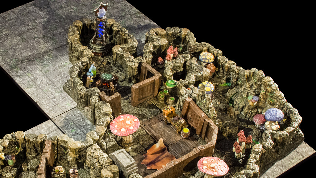 An overhead shot of an alchemist's lab built within a chamber of a cavern with workstations, a rug and fireplace, and freestanding wooden walls