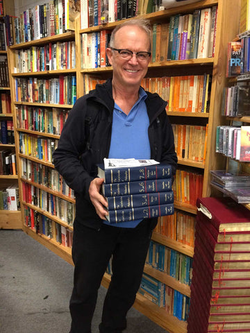 Philip Shepherd holding a stack of encyclopedias in an Irish bookstore
