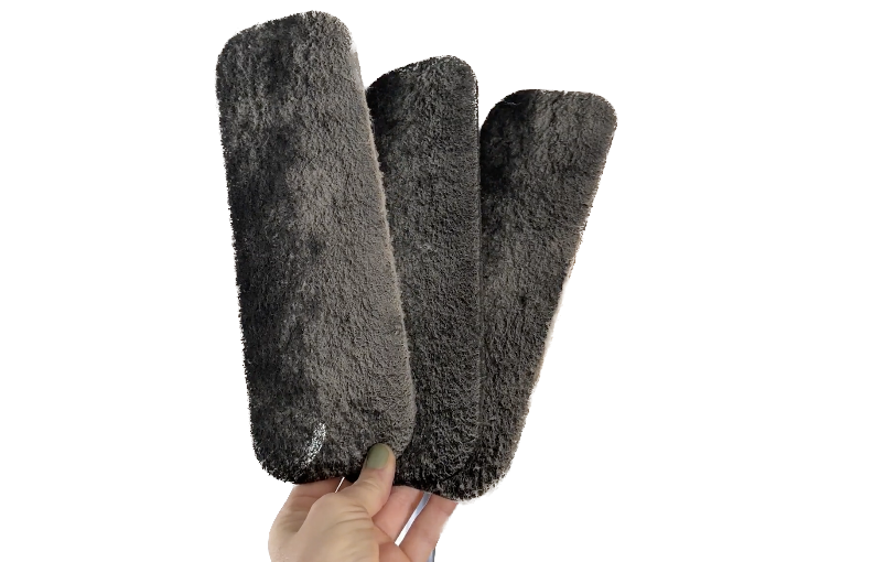 Hand holding three dark grey fuzzy scrub pads.