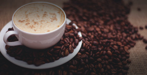 A cup of hot coffee with coffee beans splashed around