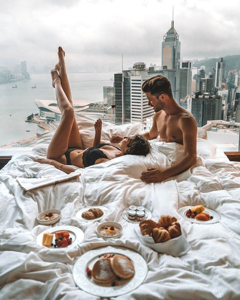 Is it Cheaper to Book All-inclusive or Separate? - Couple in a luxury hotel bed with skyline city view