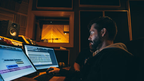 Musician making music with software on two desktops.