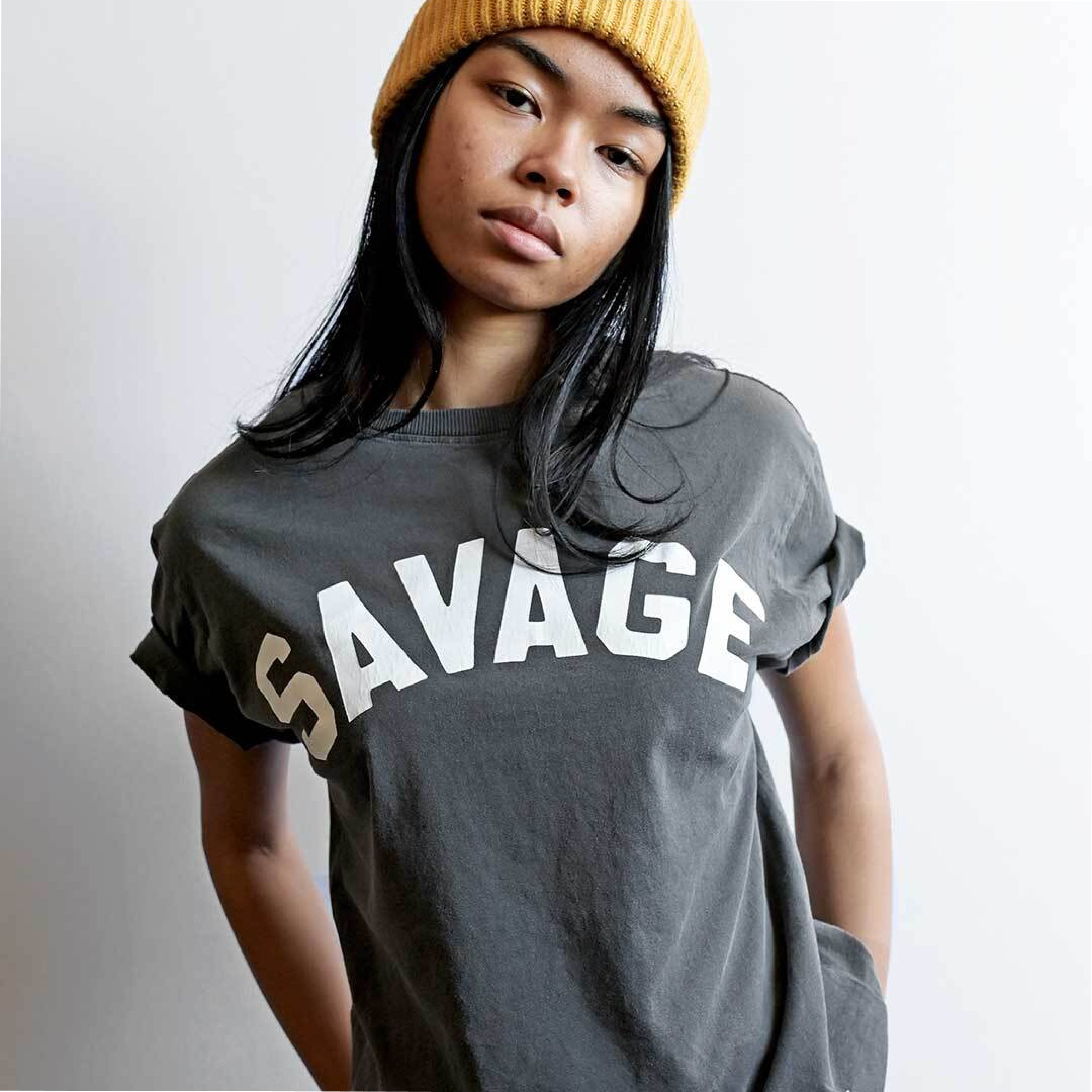 Woman wearing a yellow beanie and gray 'SAVAGE' t-shirt.