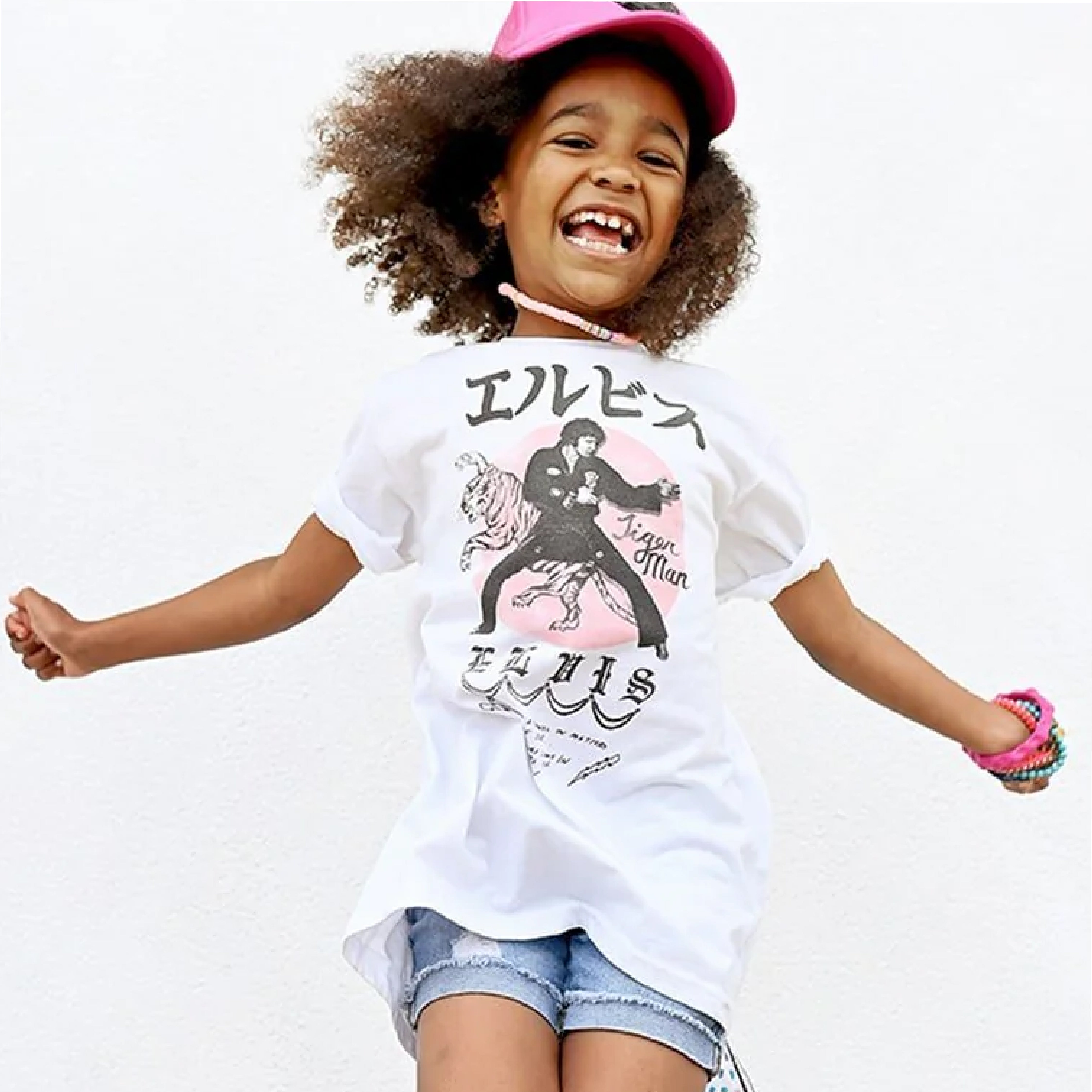 Happy young girl jumping, wearing a graphic t-shirt and a baseball cap.