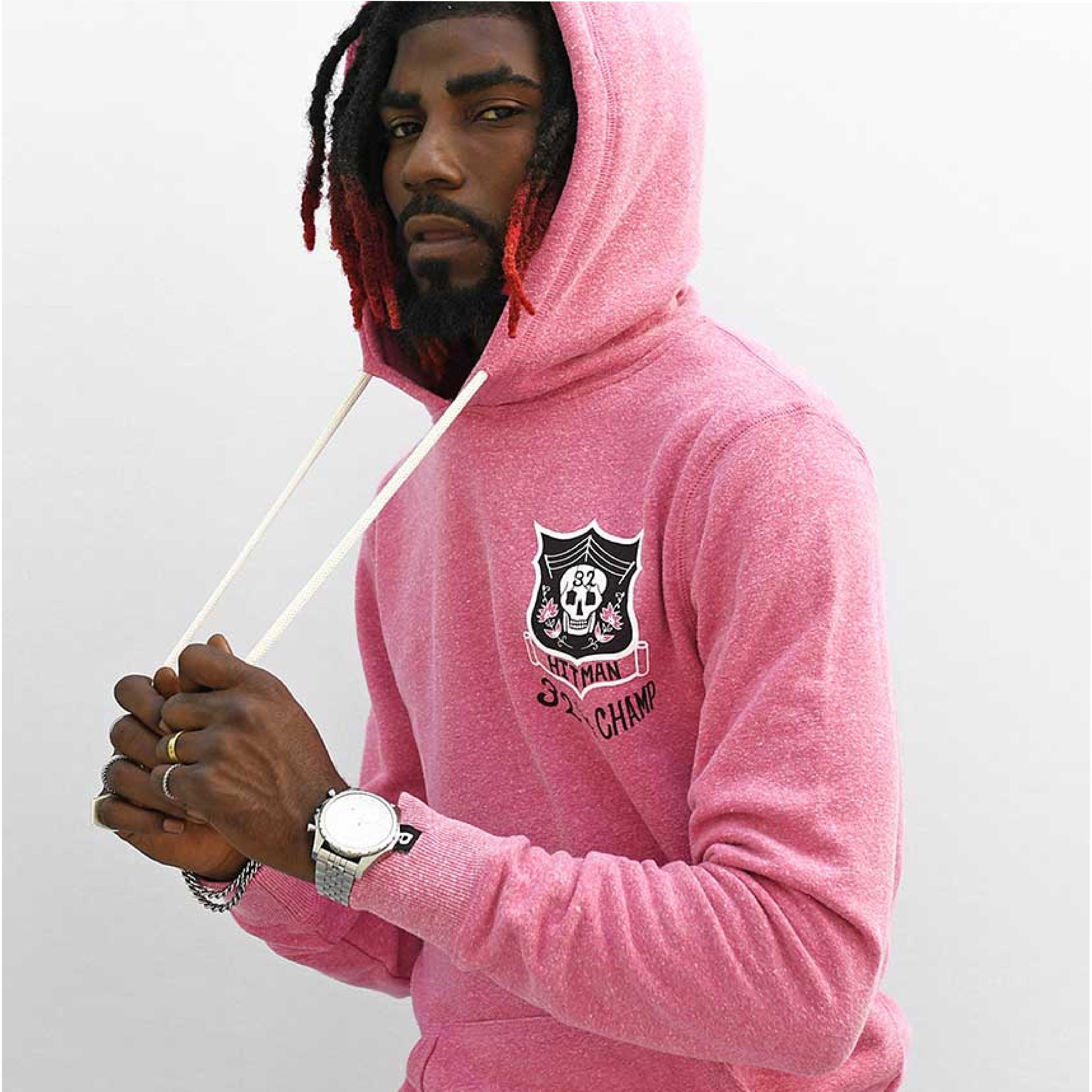 Man in pink hoodie pulling drawstring, against gray background.