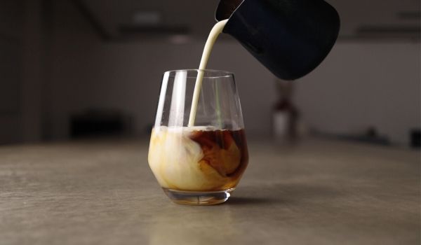pouring milk into glass of cold brew coffee