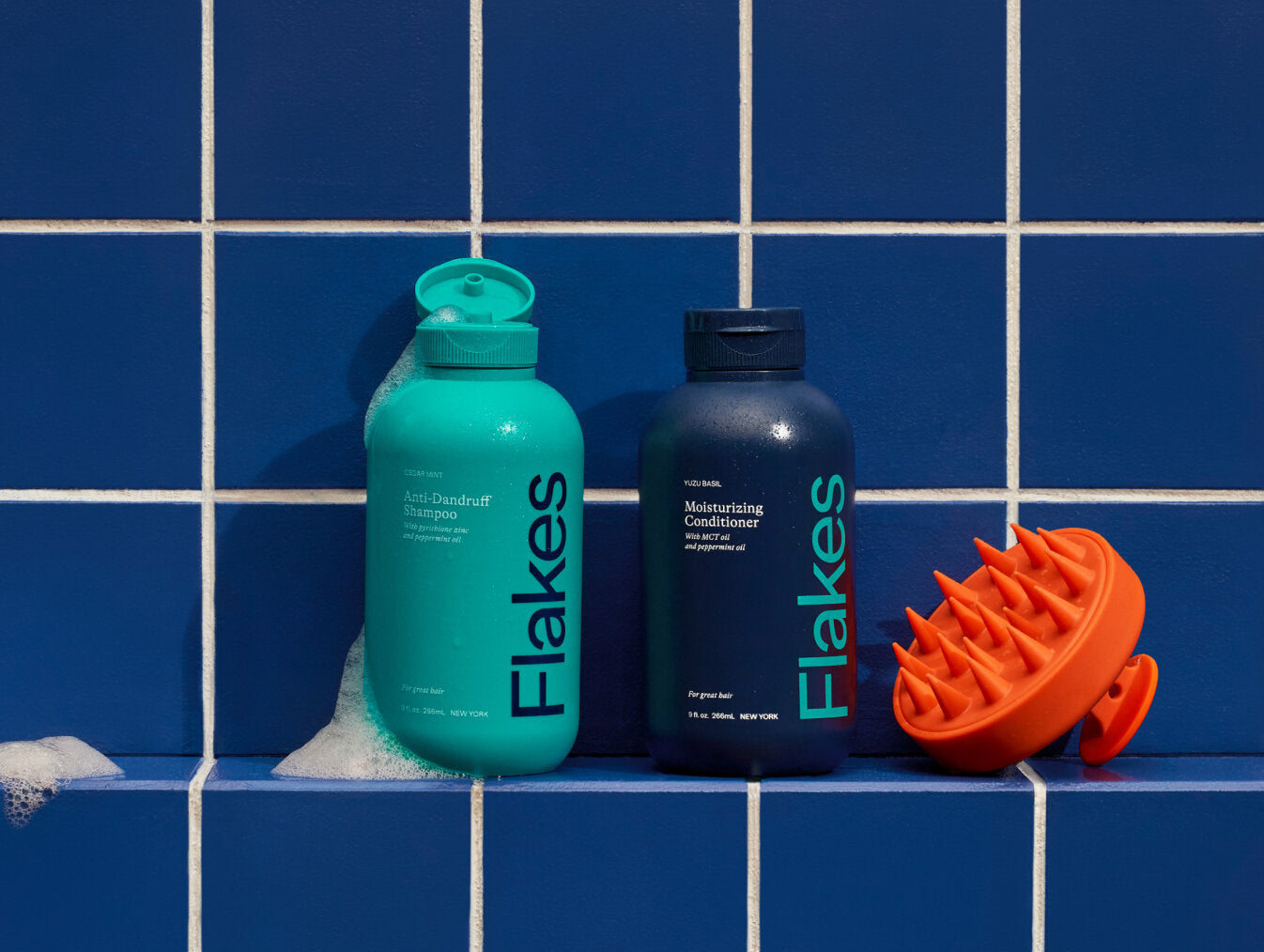 Bottles of anti-dandruff shampoo and conditioner next to an orange scalp scrubber on blue tiles.