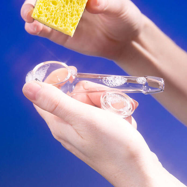 Hand cleaning a glass pipe and bowl with sponge and soap