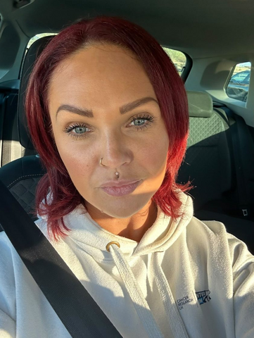 A lady with red hair poses in her car