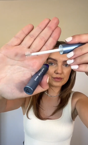 Jamie Amanda holds an open bottle of RapidBrow Eyebrow Enhancing Serum and shows off the spoolie applicator brush