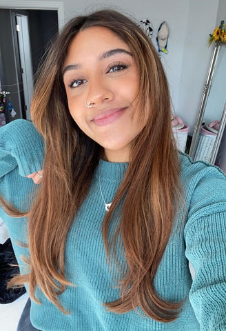 A woman with long brown hair wearing a teal jumper poses and smiles
