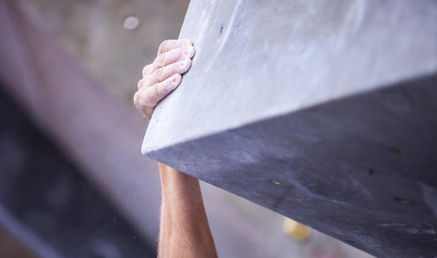 Climber throwing left hand onto the edge of a boxy hold in the gym