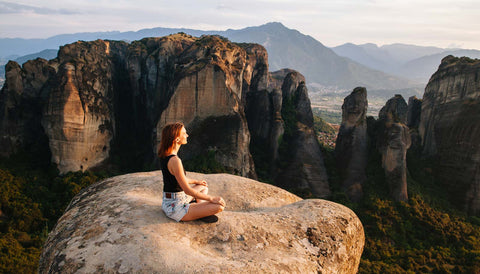 Woman meditating on top of rock with epic cliff band behind her and mountains fading away into the horizon