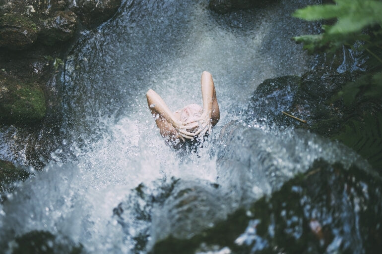 Frau duscht in Wildnis unter einem Wasserfall