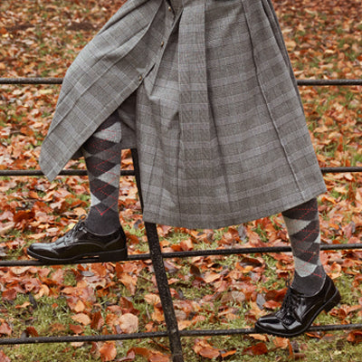 Closeup of person's legs in a tartan kilt, wearing Burlington argyle knee-high socks