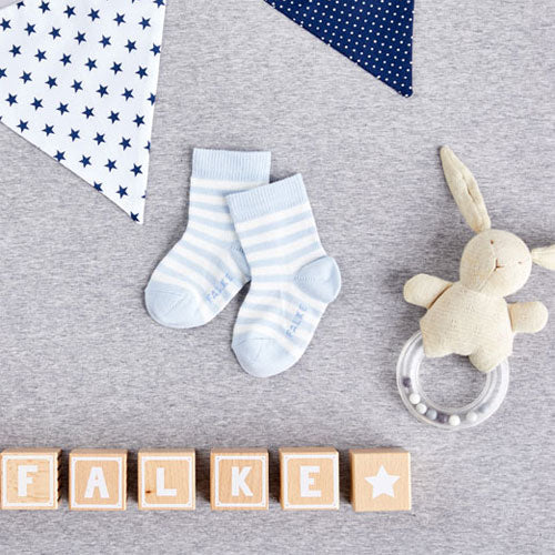 Baby socks on a grey carpet next to toy boxes spelling out 'Falke'