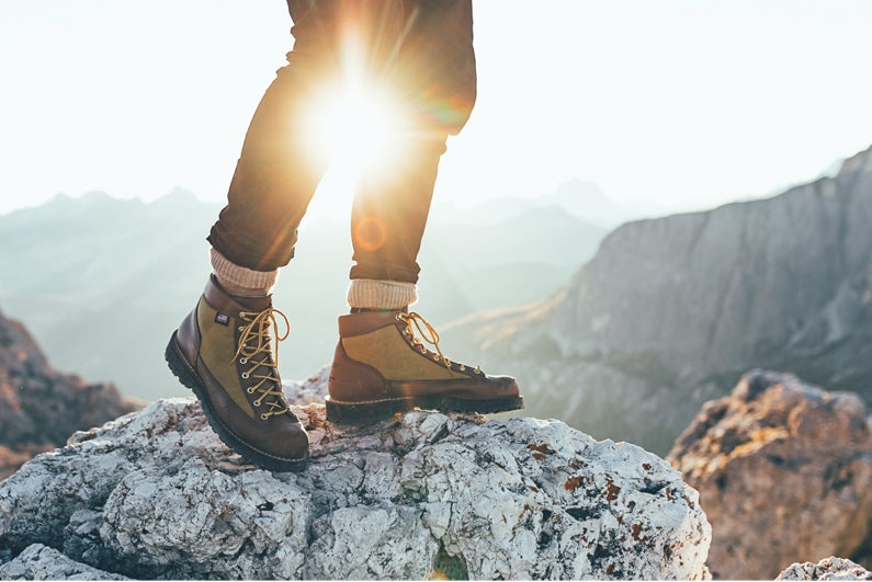 Person wearing Falke TK4 trekking socks, standing outside on a rocky range, sun in background