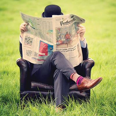 Man sitting in chair in a field, reading Pantherella newspaper 