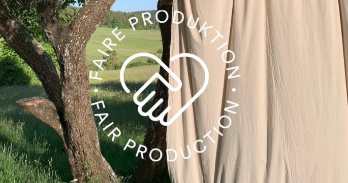 Clothing material hanging on a wire outside next to a tree, overlay says 'Fair Production' with accompanying logo