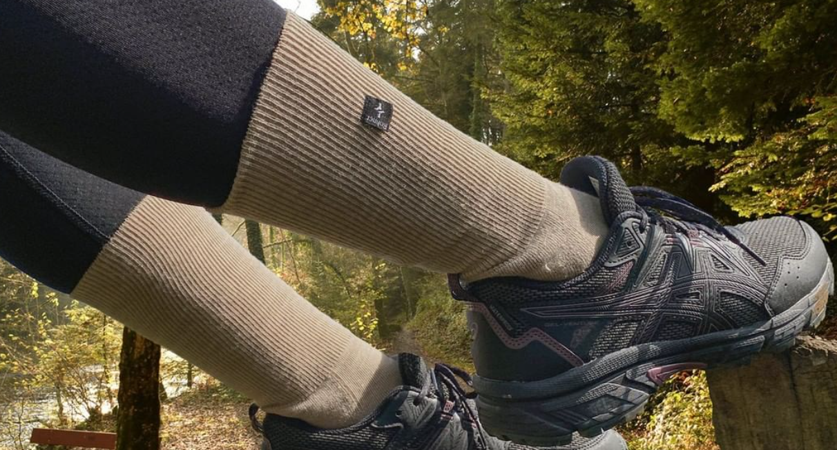 Closeup of person's legs - wearing Rohner socks, set against a nature backdrop of green trees, fallen leaves and a wooden bench