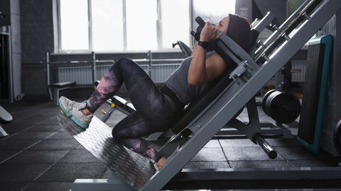 Female athlete doing lunges in hack squat gym machine, copy space