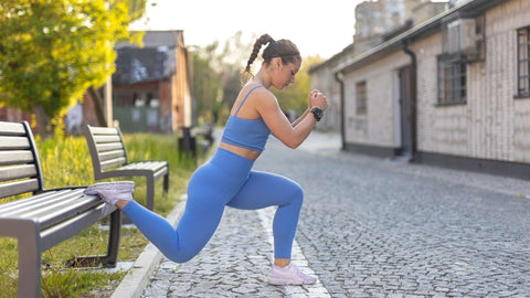 Young fitness female model in blue training sportswear doing single leg split squats on bench in street city valley