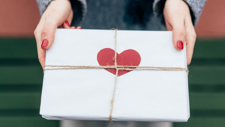 hands holding a white parcel with a red heart