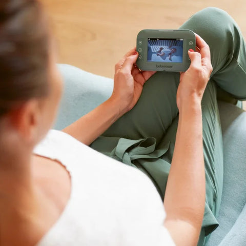 Lifestyle photo of a mother holding her babymoov yoo master monitor to see her little one. The image is set from a point-of-view angle as if you are in the place of the mother holding the monitor.