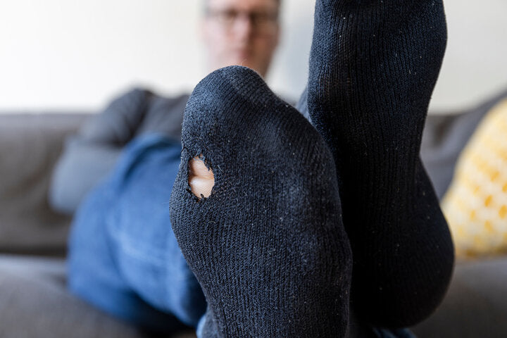 A man sits on a grey sectional couch with his feet up on the furniture.